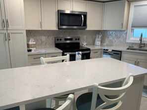 A modern kitchen with white cabinets, a black microwave, stainless steel appliances, and a marble countertop. - IT'S A SHORE THING - 
ON THE BEACH - SPECTACULAR SUNSETS
NEWLY RENOVATED (Fort Myers Beach)
