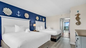 A hotel room with two beds, a seahorse wall decoration, and a view of the sea through an open door. - Compass Cove 366 (Myrtle Beach)