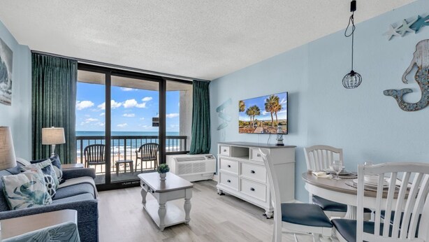 A living room with a balcony, a dining area, and a painting on the wall. - Compass Cove 366 (Myrtle Beach)