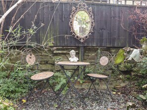 A garden with two metal tables, a stone wall, and a decorative mirror. - Heathcliff Cottage (Keighley)