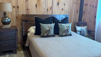 A bedroom with a wooden wall, a bed with a white quilt, and three pillows with owl designs.