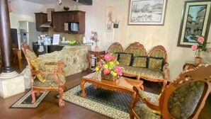 A living room with a sofa set, wooden chairs, a coffee table, and a kitchen in the background. - Villa in Santa Inés condominium, a few meters from the entrance to Antigua Guatemala. (Santa Inés del Monte Pulciano)
