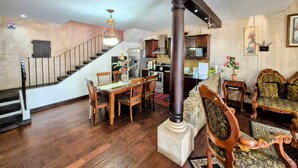 A spacious living area with a wooden dining table, chairs, a staircase, and a kitchen in the background. - Villa in Santa Inés condominium, a few meters from the entrance to Antigua Guatemala. (Santa Inés del Monte Pulciano)