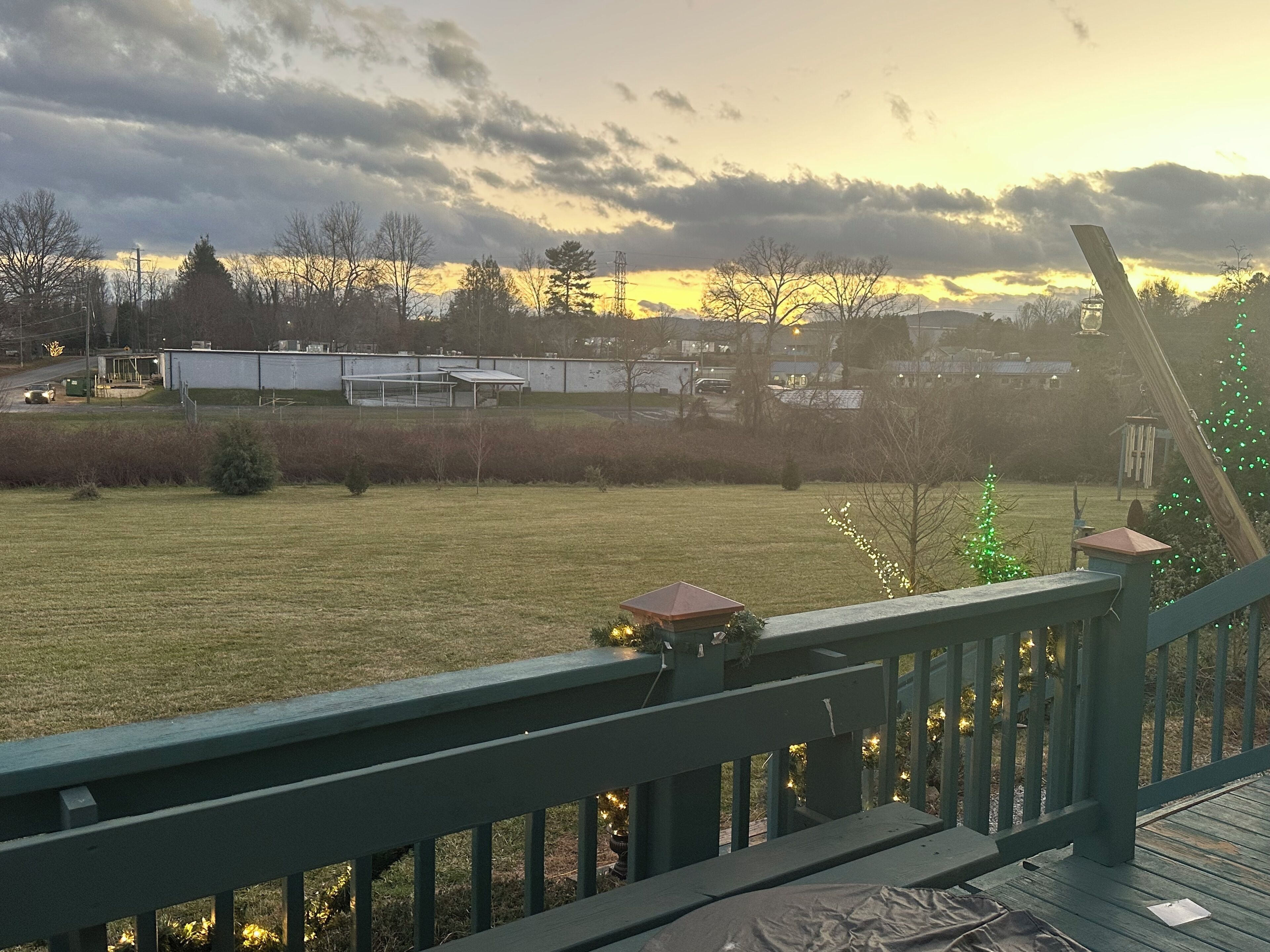 Vista de um deck com vista para um campo gramado e um pôr do sol ao fundo.