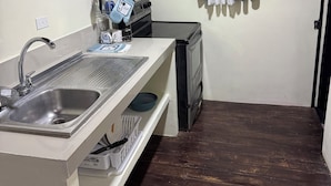 Une cuisine de taille réduite, équipée d’un évier, d’une cuisinière et d’une fenêtre avec des rideaux.