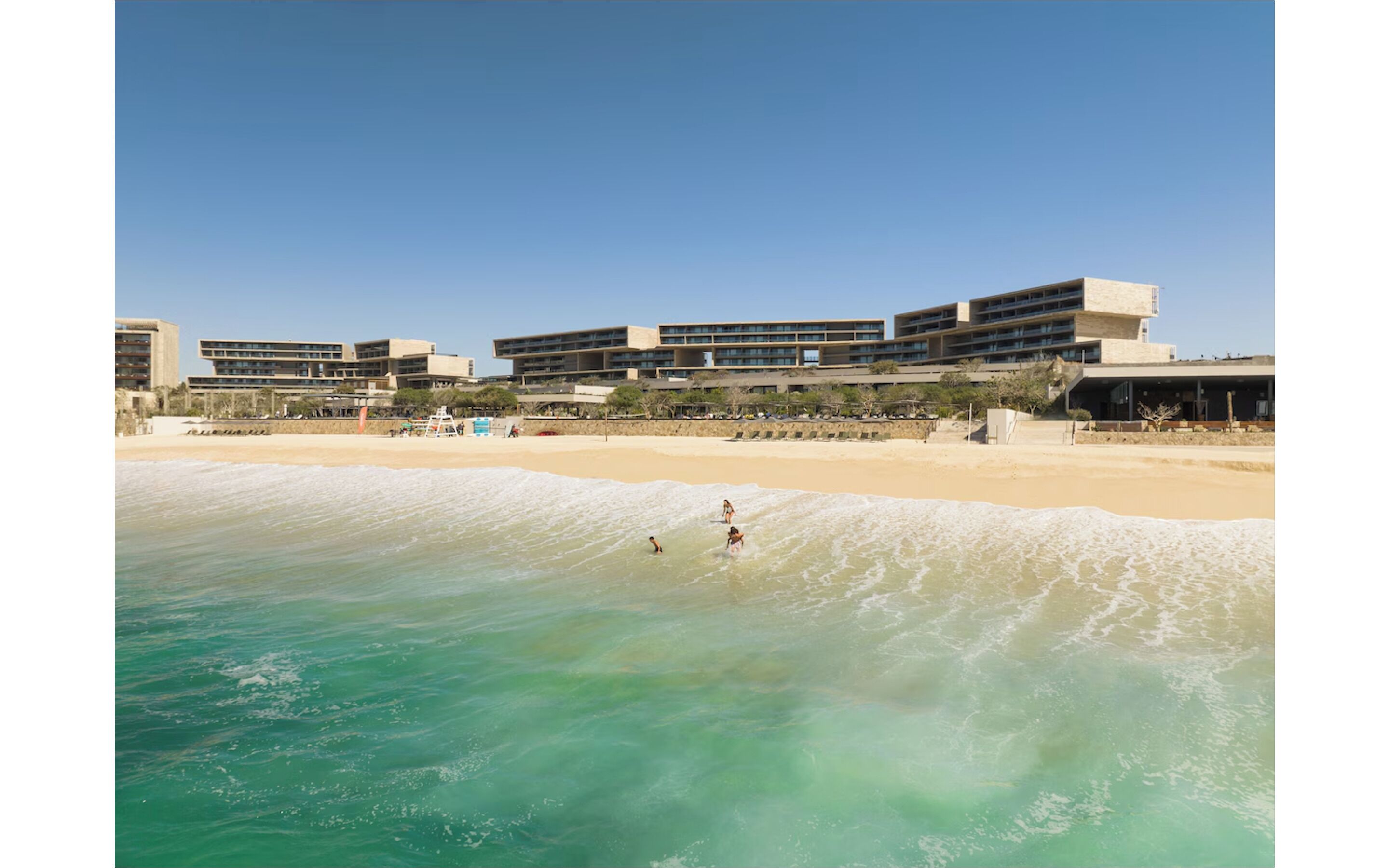 Un hôtel situé en bord de mer, composé de plusieurs bâtiments, avec une plage de sable fin et une eau cristalline.
