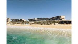 Un hotel frente a la playa con varias construcciones, una playa de arena y agua azul cristalina.