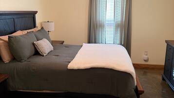 Ein Schlafzimmer mit Bett, Nachttisch, Lampe, Deckenventilator und einem Fenster mit Vorhängen.