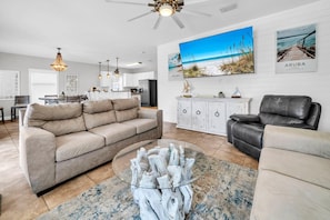 A modern living room with a beige sofa, a glass coffee table, a leather recliner, and a dining area with a white cabinet and pendant lights. - Aruba (Miramar Beach)