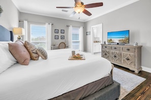 A bedroom with a large bed, a ceiling fan, a television, and a view of the beach through the window. - Curacao (Miramar Beach)