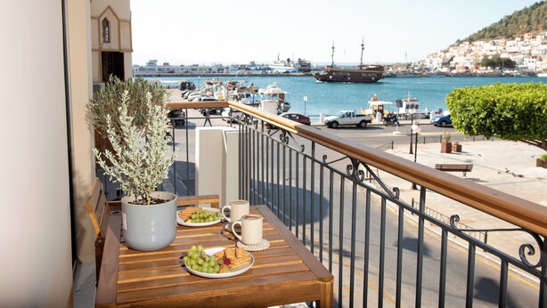 Ein Balkon mit Holztisch, gedeckt für ein Frühstück, mit Blick auf einen Hafen, Boote und eine Stadt im Hintergrund.
