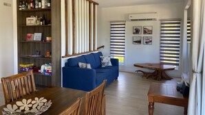 A modern living room with a blue sofa, wooden dining table, and a built-in bookshelf. - Chalet L'Ancrage; anchoring yourself in nature! (Grandes-Piles)