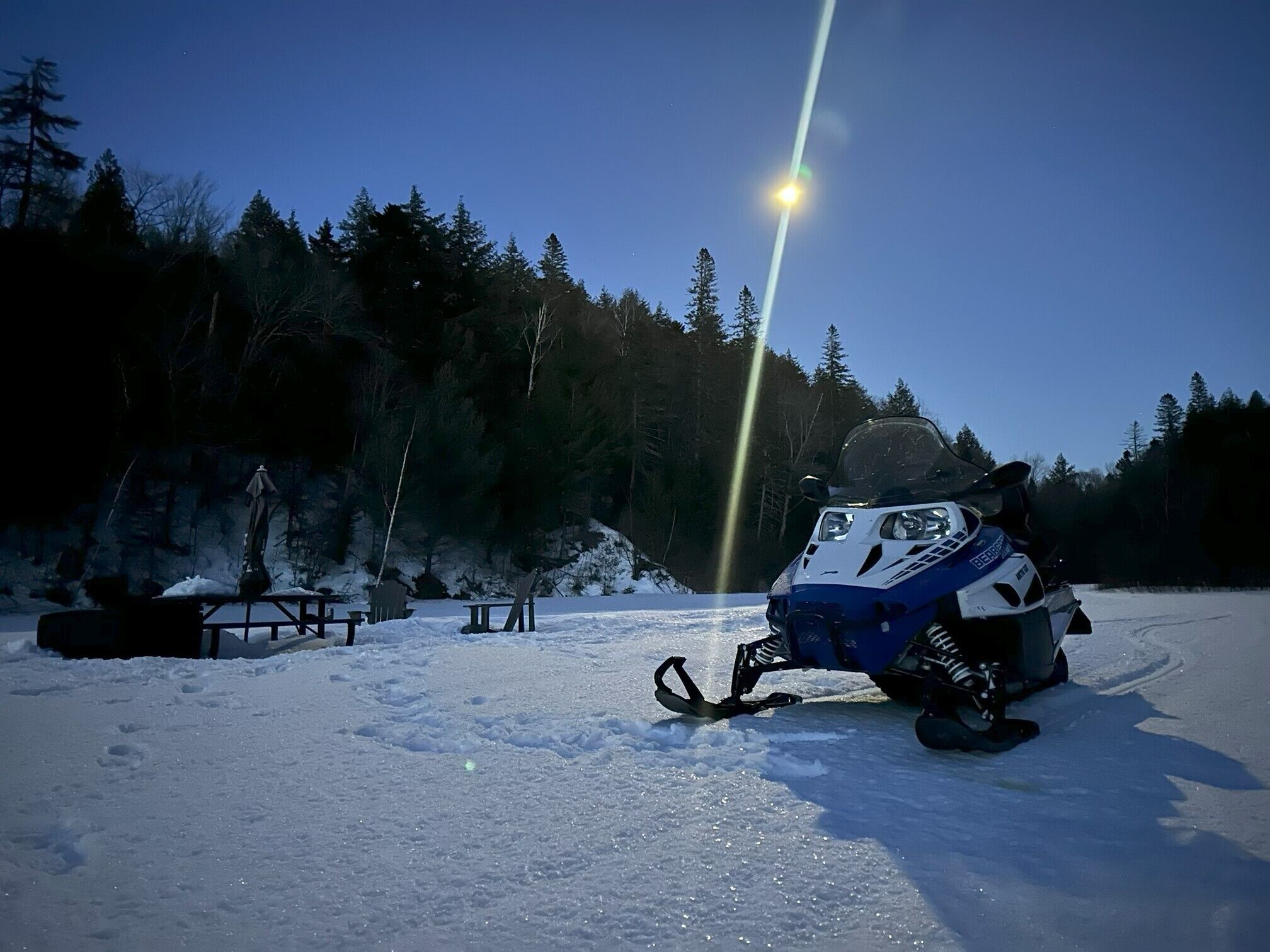 A snowmobile parked in a snowy area with a clear sky and a light source in the background.