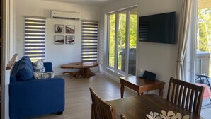 A modern living room with a blue sofa, wooden dining table, and large windows with blinds. - Chalet L'Ancrage; anchoring yourself in nature! (Grandes-Piles)
