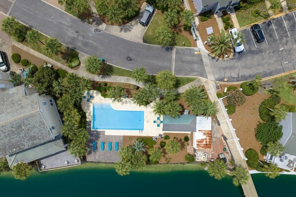 An aerial view of a property with a swimming pool, palm trees, and a road. - Nana's Beach House (Destin)