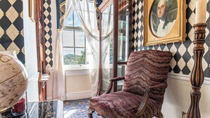 Una habitación con pared estampada, un ventanal con cortinas, un globo terráqueo sobre una mesa y un retrato enmarcado.