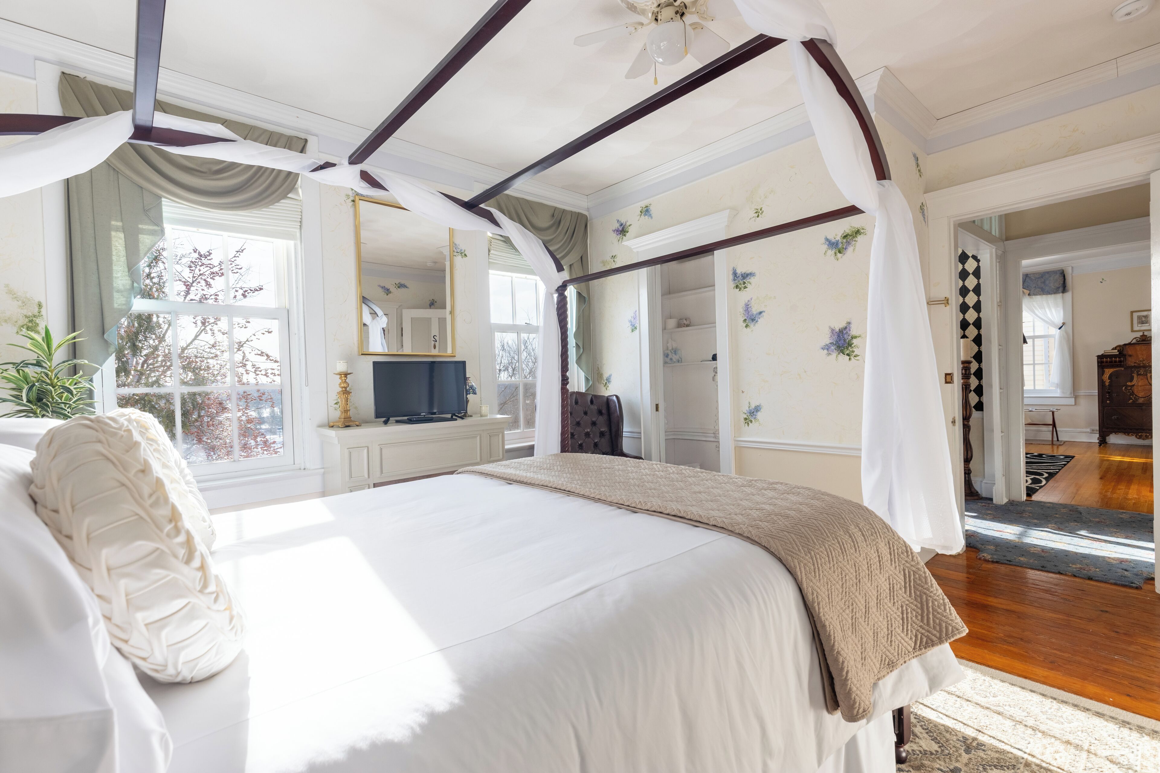 A spacious bedroom with a large bed, a ceiling fan, and a view of the outdoors through a window.