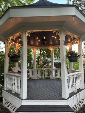A gazebo with a wooden deck, white railings, and hanging flower baskets. - Miss Murphy's High Street Inn (Galena)