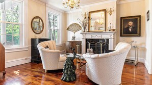 Una sala formal con dos sillones, una chimenea, un espejo y una araña.