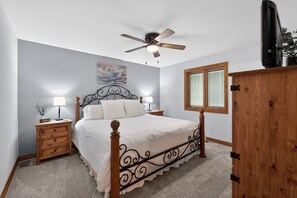 A bedroom with a bed, nightstands, a ceiling fan, a window, and a wooden wardrobe. - Indian Point Waterfront Home w/ Wraparound Deck (Garfield)