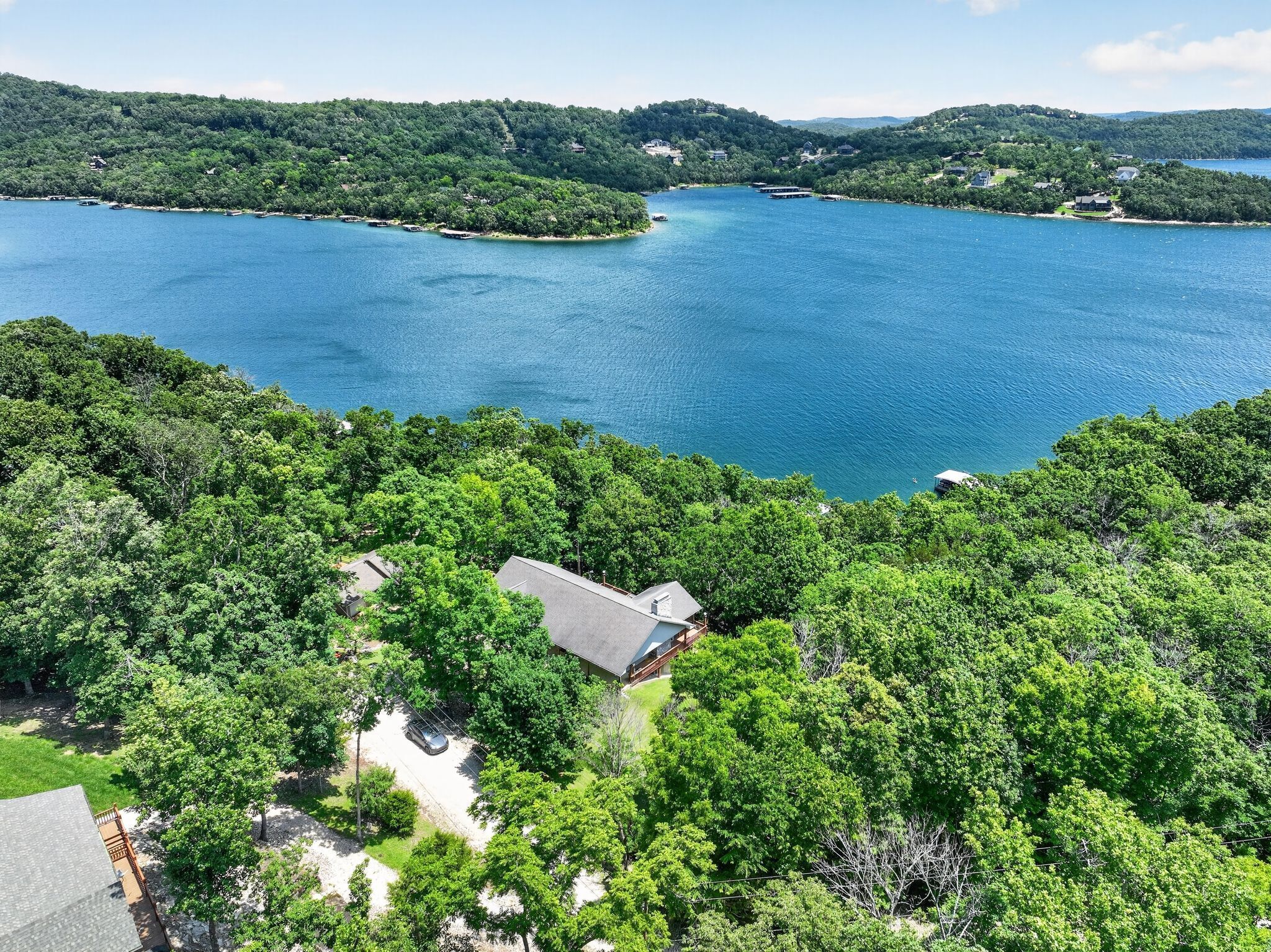 A lakeside property with a house surrounded by dense trees, a dock, and boats.