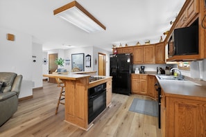 A modern kitchen with wooden cabinets, a black refrigerator, and a built-in island with a stove. - Indian Point Waterfront Home w/ Wraparound Deck (Garfield)