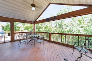 A covered outdoor deck with a table and chairs, a railing, and a view of trees. - Indian Point Waterfront Home w/ Wraparound Deck (Garfield)