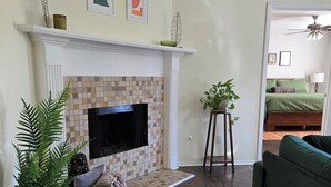 Una sala de estar con chimenea, televisor, sofá verde y planta en maceta.