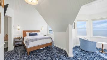 Un dormitorio con cama, mesita de noche, lámpara y vista al mar.