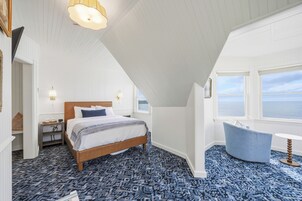 Un dormitorio con cama, mesita de noche, lámpara y vista al mar.