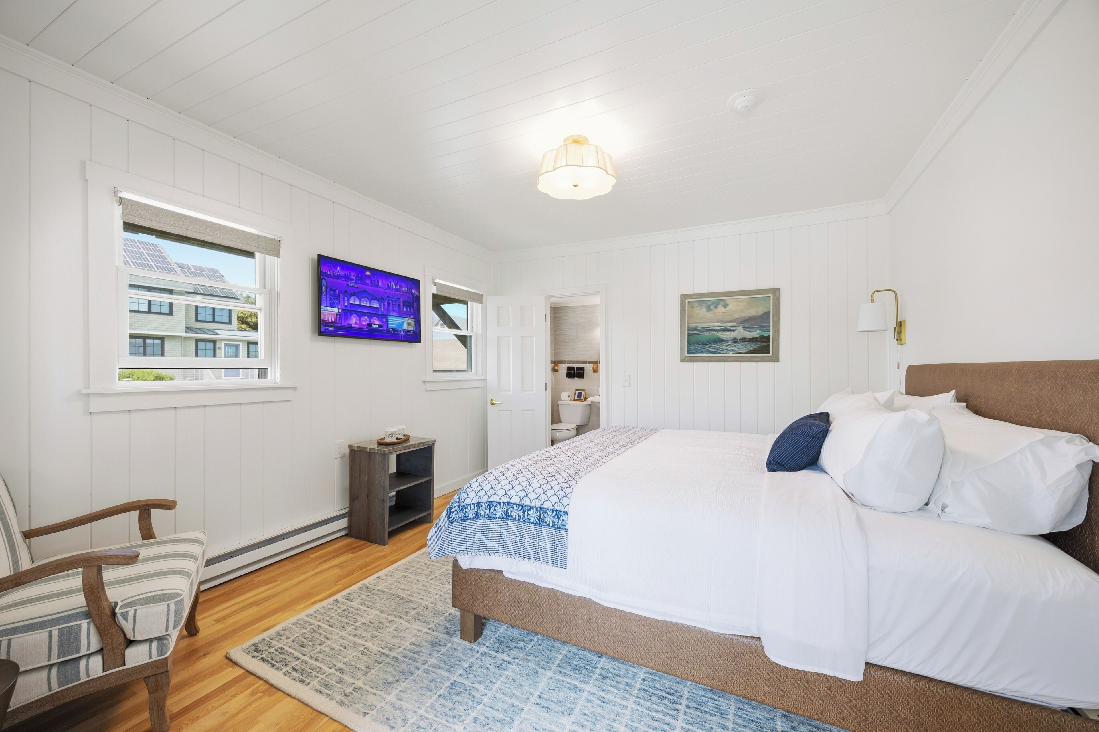 A bedroom with a bed, a chair, a television, a window, and a door.