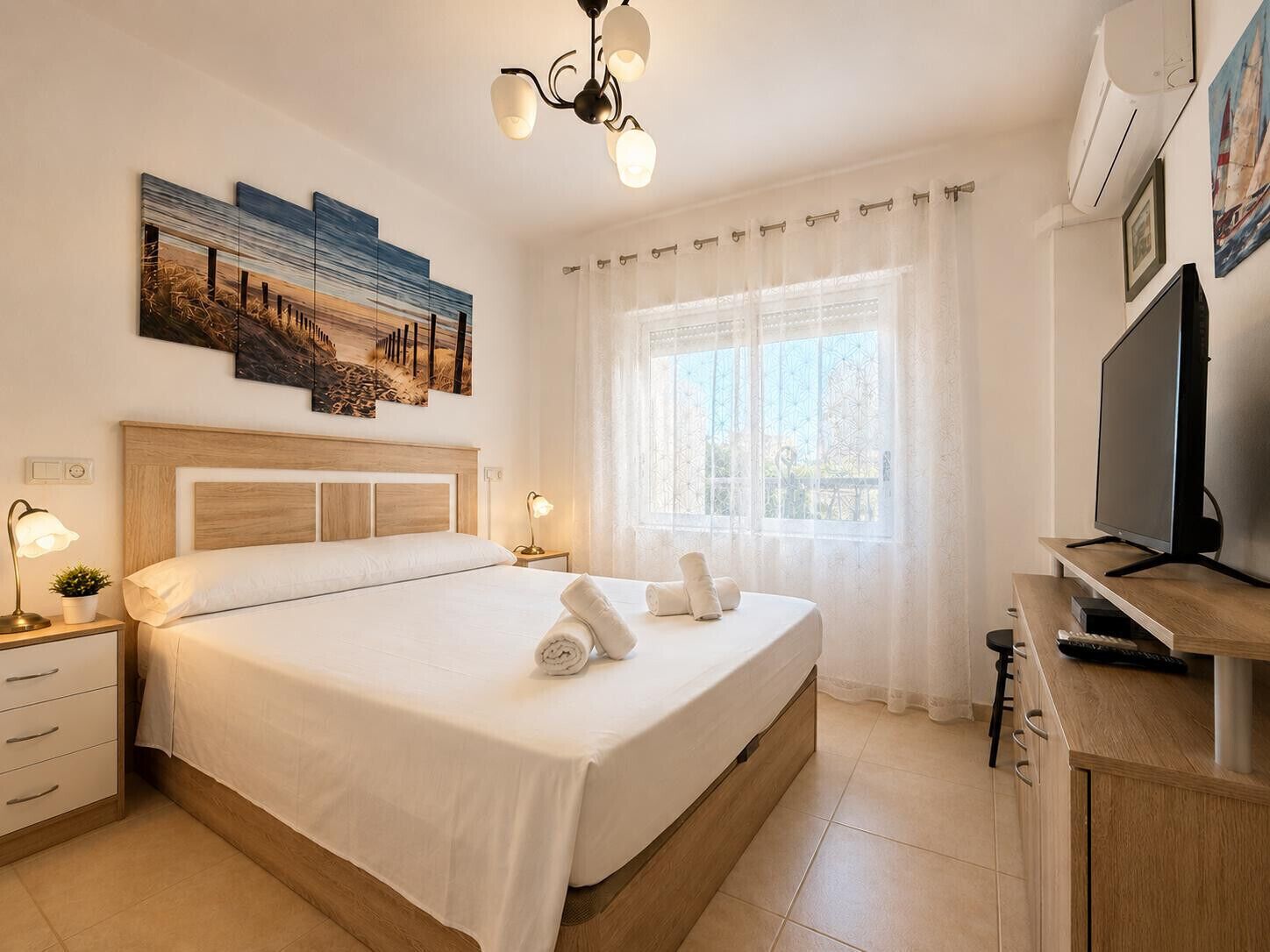 Hotellihuone, jossa on sänky, yöpöydät, televisio ja taideteoksia seinällä.