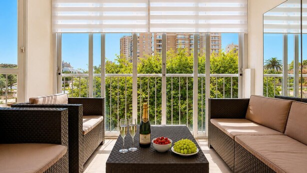Ein Balkon mit Korbmöbeln, einem Tisch, einer Champagnerflasche, Gläsern und Obst.