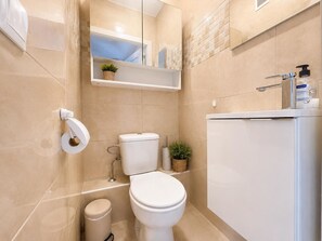 A bathroom with a toilet, a small trash bin, a shelf with a plant, and a mirror. - SUNNY GEMINIS (Calpe)