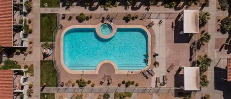 An aerial view of a hotel with a central swimming pool, lounge areas, and a covered patio.