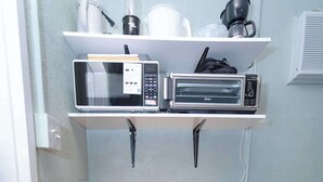 A compact kitchen with a microwave, toaster, and coffee maker on a shelf, and a cabinet with a rice cooker and slow cooker underneath. - Private Suite | Comfortable, Quiet & Well-Equipped (Augusta)