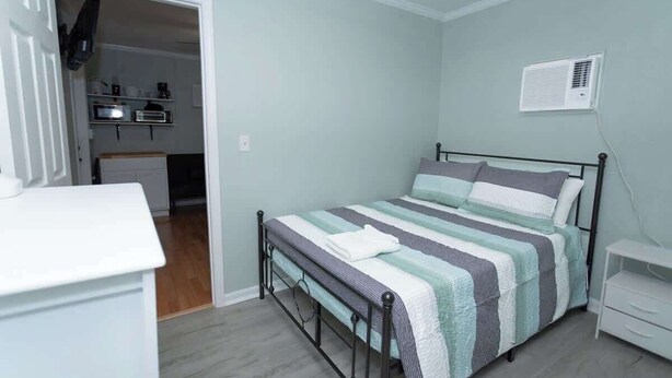 A bedroom with a bed, bedside table, and a small white cabinet. - Private Suite | Comfortable, Quiet & Well-Equipped (Augusta)