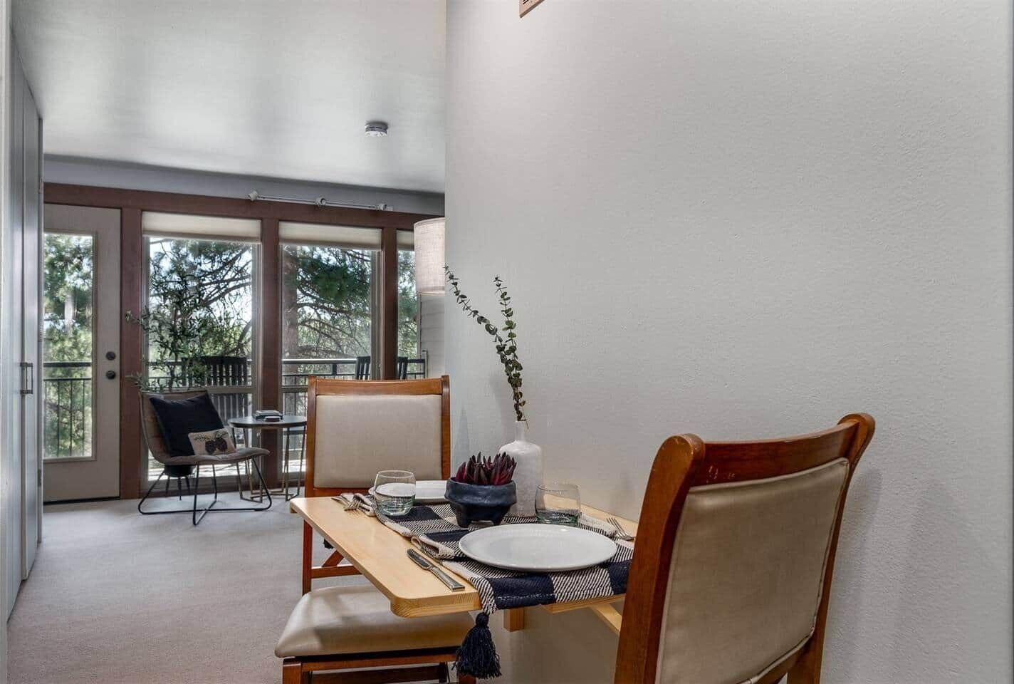 A dining area with a table set for two, chairs, a view of the outdoors, and a balcony.