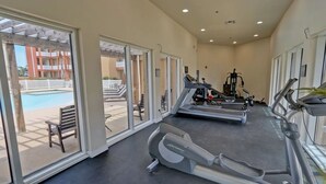 Et fitnesscenter med løbebånd, en motionscykel og et vægttræningsmaskine. Der er en bænk og en stol udenfor fitnesscenteret.