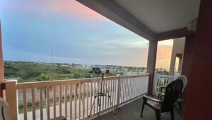 En balkon med et teleskop, stole og udsigt over et kystlandskab.