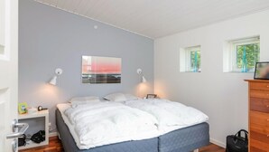 Un dormitorio con cama, lámparas de noche, ventana, cómoda y un cuadro en la pared.