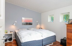 Ein Schlafzimmer mit Bett, Nachttischlampen, einem Fenster, einem Schminktisch und einem an der Wand hängenden Bild.