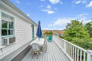 Une terrasse couverte avec une table et des chaises, un parasol bleu et une balustrade blanche.