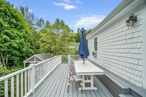 Une terrasse avec une table et des chaises, entourée d’une balustrade blanche, et un parasol bleu.