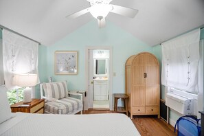 Een slaapkamer met een bed, een stoel, een kledingkast, een bureau en een plafondventilator.
