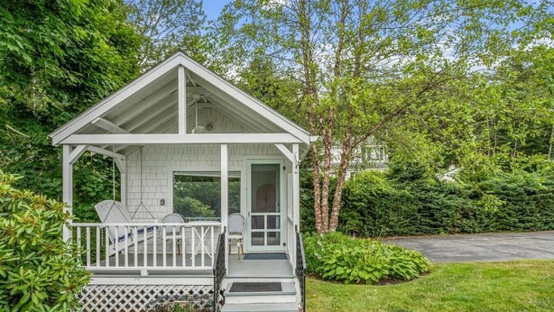 Une petite maison blanche avec un porche, un escalier et une porte.