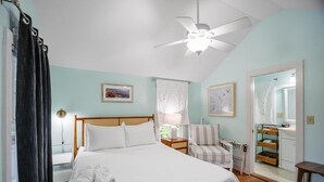 A bedroom with a bed, a chair, a bedside table, a ceiling fan, and a bathroom mirror.