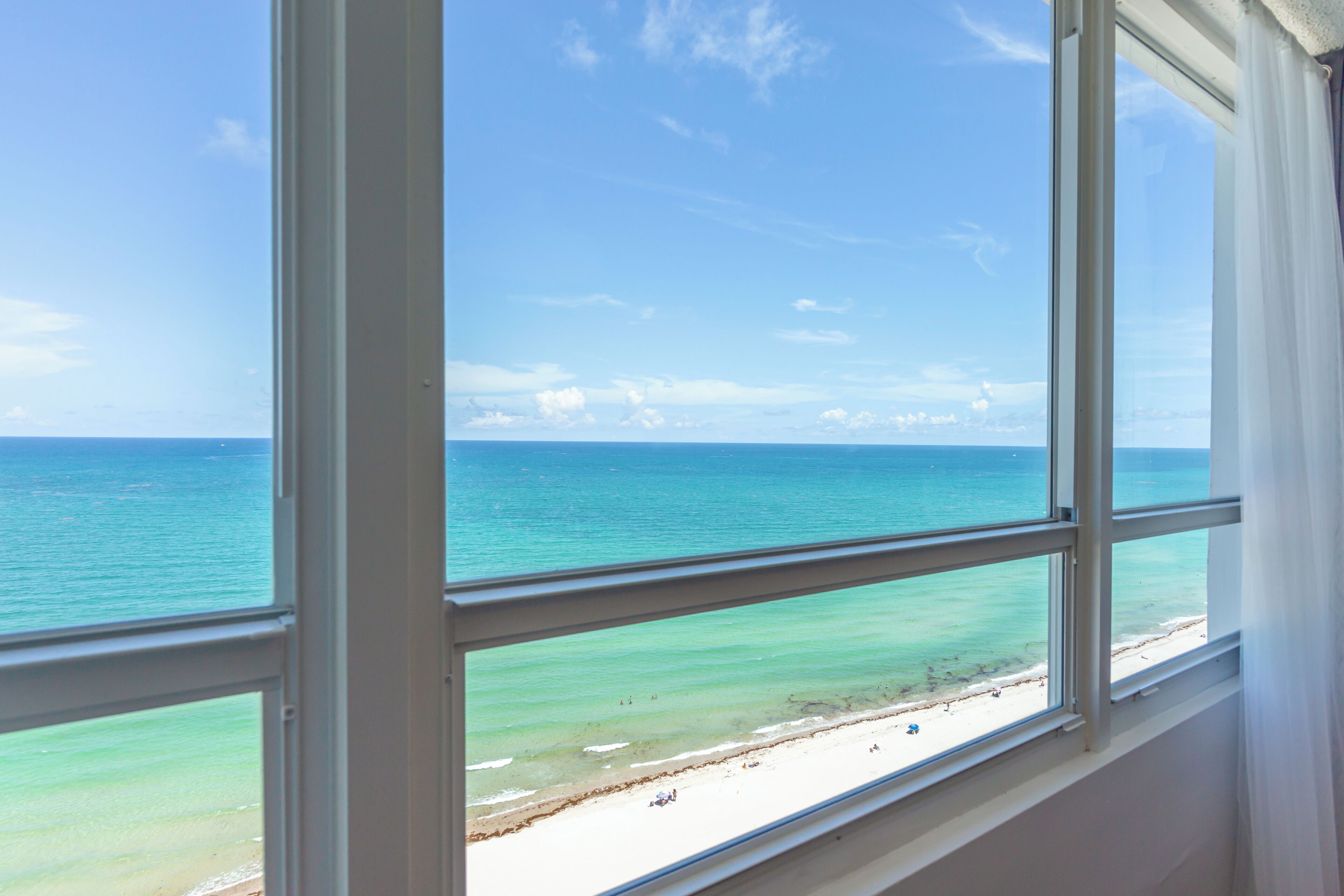 A view through a window of a beach with clear blue water and a sandy shore.