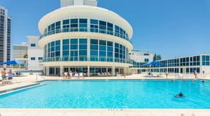 A hotel with a large pool, a covered area with lounge chairs, and a modern building with multiple windows. - Boutique Apartments Castle Beach (Miami Beach)