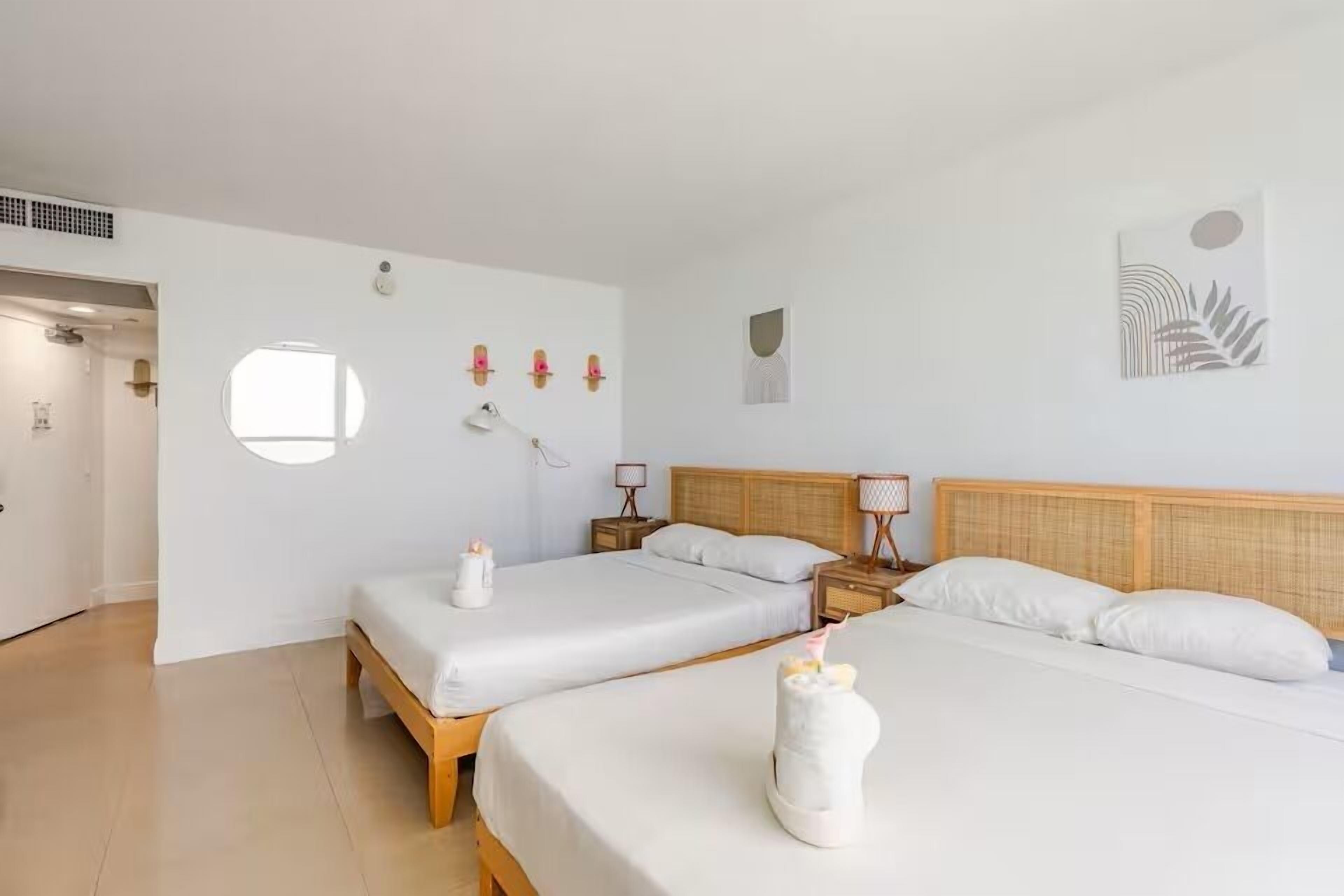 A hotel room with two beds, a round window, wall art, and a door leading to another room.
